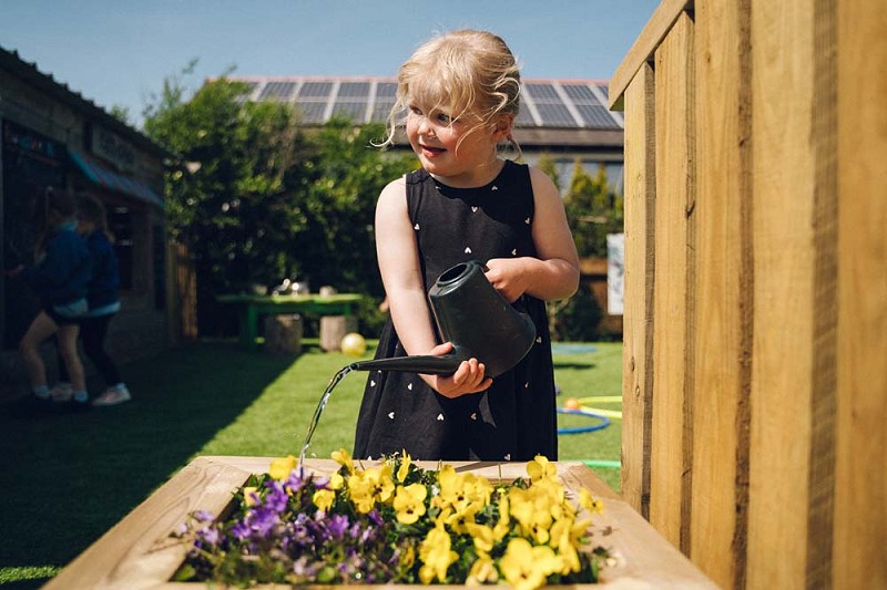 merch ifanc yn rhoi dwr i flodau melyn a piws